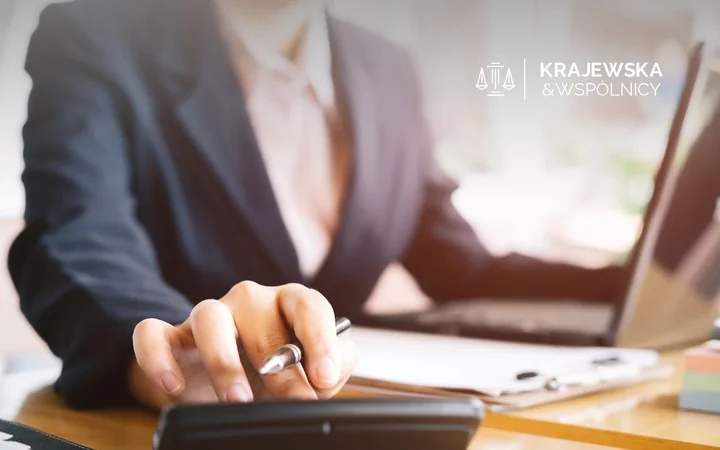 Osoba w garniturze liczy przy biurku z laptopem i kalkulatorem.