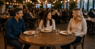 Trzy osoby siedzą przy okrągłym stole w restauracji, rozmawiając przy posiłku.