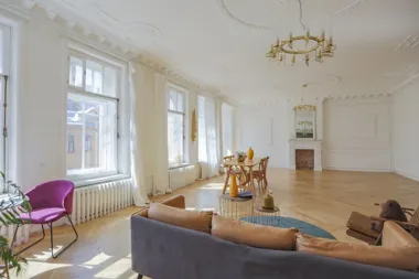 Jasny, przestronny salon z dużymi oknami, drewnianą podłogą, sofą, stołem i kominkiem.