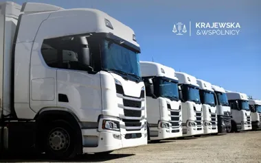 Rząd białych ciągników siodłowych zaparkowanych na placu pod bezchmurnym niebem.