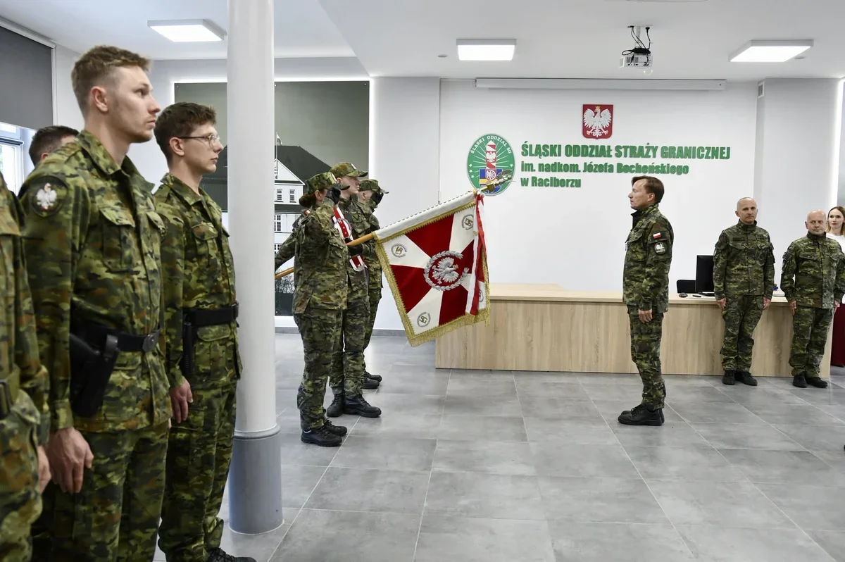 Żołnierze Straży Granicznej w mundurach stoją w sali z flagą podczas uroczystości w siedzibie Śląskiego Oddziału Straży Granicznej w Raciborzu.
