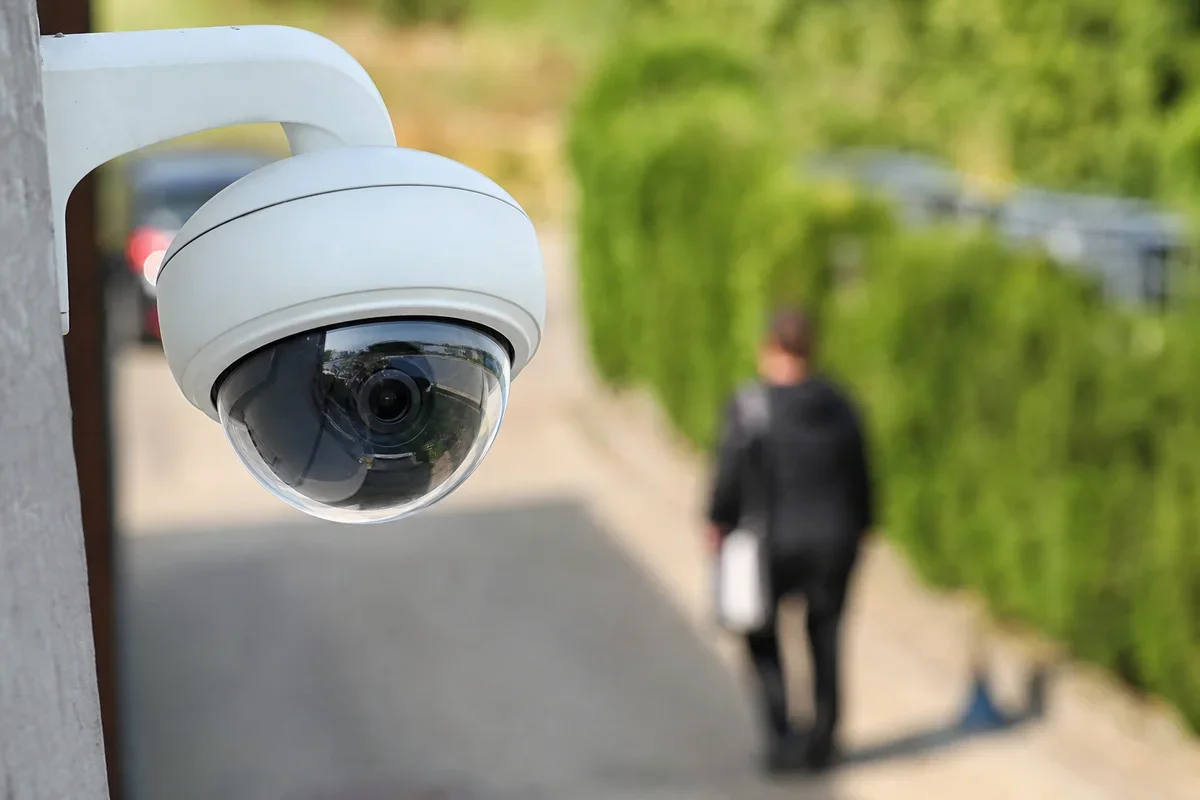 Kamera monitoringu zamontowana na elewacji budynku filmuje chodnik, po którym przechodzi mężczyzna w garniturze z teczką.