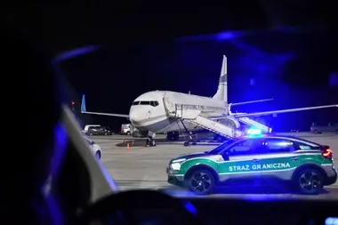 Samolot pasażerski stoi na lotniskowym pasie nocą, obok przejeżdża pojazd Straży Granicznej z włączonymi światłami.
