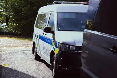 Policyjny furgon z napisem „POLICIE” stoi na drodze obok innego pojazdu, w tle widać zadrzewiony teren.