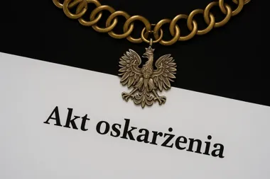 Fragment łańcucha z orłem w koronie leży na białym dokumencie z napisem „Akt oskarżenia” na czarnym tle.
