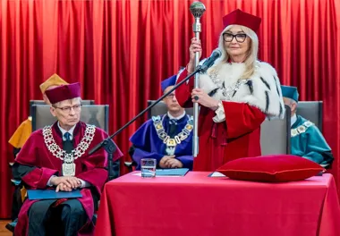 Uroczysta inauguracja roku akademickiego z rektorem w togi trzymającym berło, na tle czerwonej kurtyny.